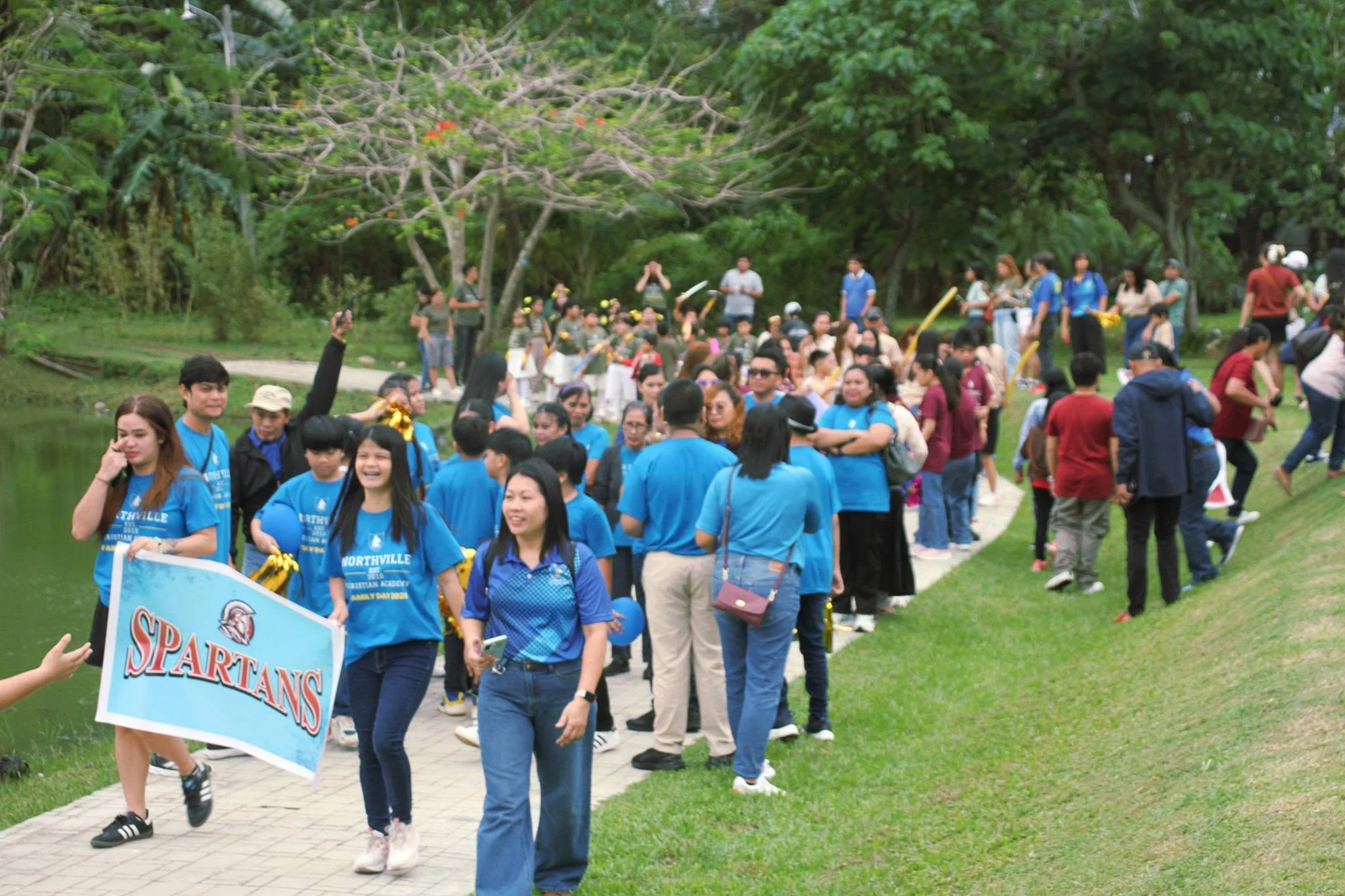 Students parade outdoors behind a "Spartans" team banner during intramurals, with a large crowd looking on.