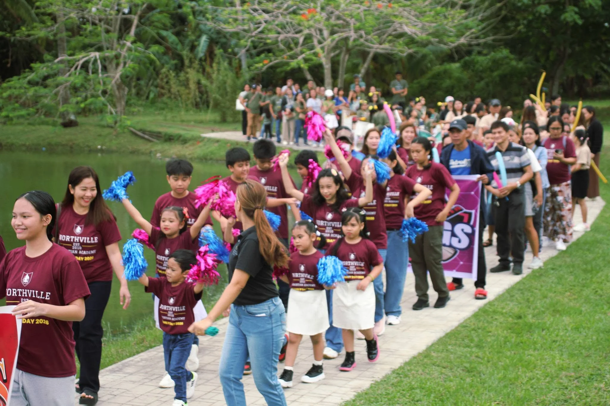 A large outdoor procession of students carrying pom-poms winds across the school grounds during intramurals.