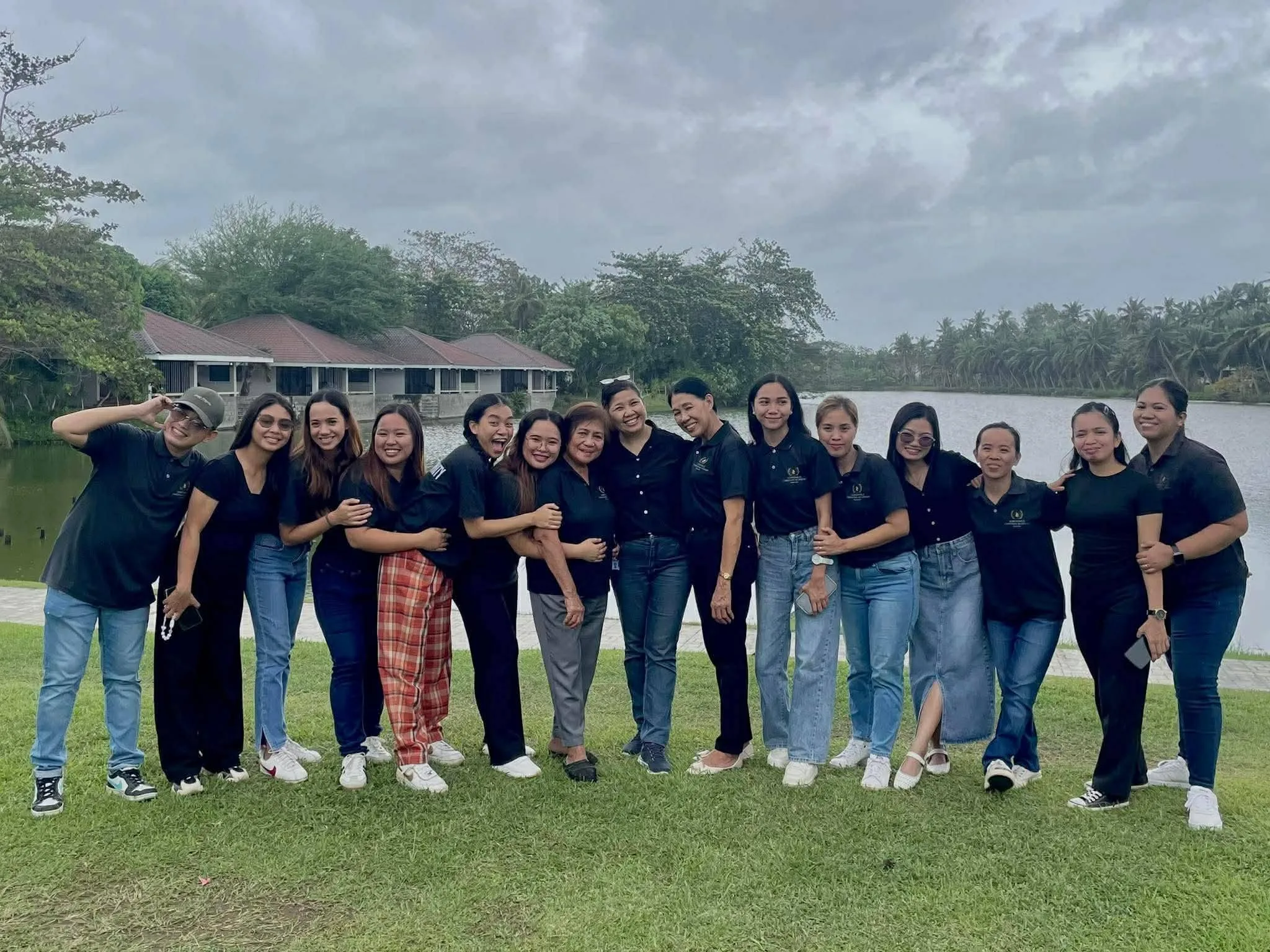 The Northville Christian Academy staff standing together on the grass beside a lake, wearing matching black school polos.